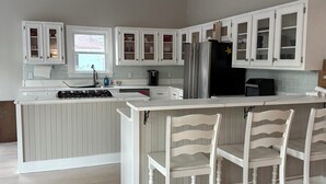 A modern kitchen with white cabinetry, a central island with bar stools, and a black refrigerator. - Pink Paradise aka The Purple House (Daufuskie Island)