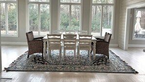 A dining area with a table and chairs, large windows, and a patterned rug. - Pink Paradise aka The Purple House (Daufuskie Island)