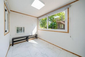 Quarto com um banco, janela com vista para árvores e um prédio, e um claraboia.