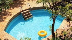 Une piscine ronde entourée d’une terrasse en bois et accessible par un escalier en bois menant à l’eau.