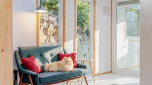 Une pièce chaleureuse avec un canapé vert, un petit chien et une fenêtre donnant sur un paysage verdoyant.