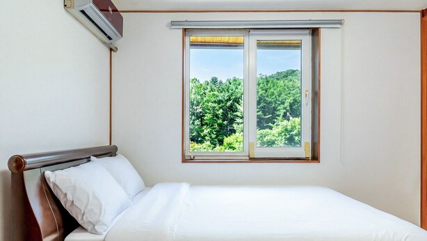 A bed with white bedding, a wooden headboard, and a window with a view of greenery. - Gapyeong Ruba Pension (Gapyeong)