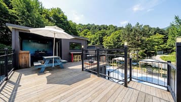 Una terraza de madera con zona de barbacoa, espacio de estar cubierto y piscina.