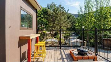 A deck with a barbecue grill, wooden stools, and a table.