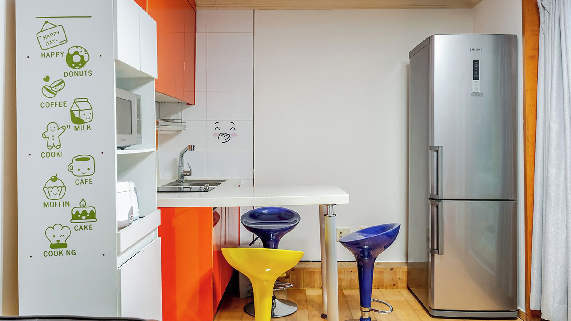 A modern kitchen with a stainless steel refrigerator, a white countertop, and a colorful bar stool.