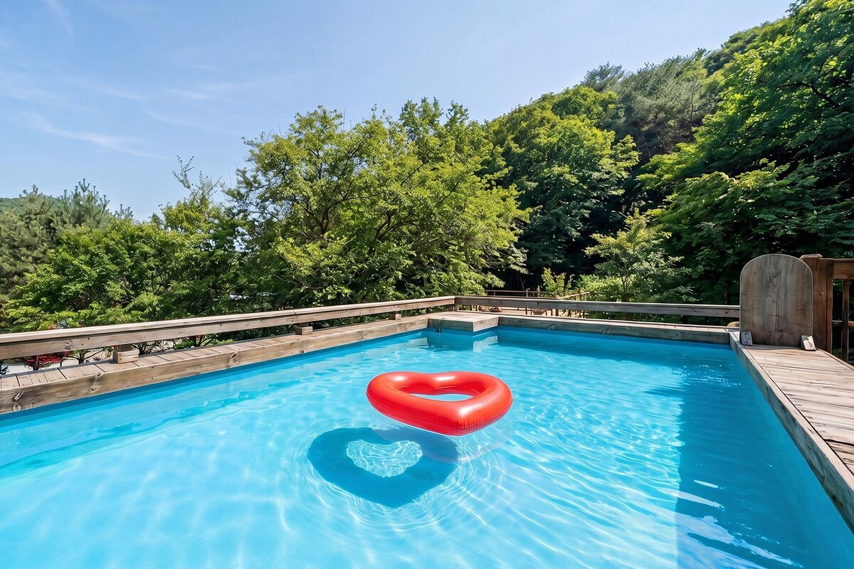 Une piscine rectangulaire avec une terrasse en bois et un flotteur en forme de cœur.