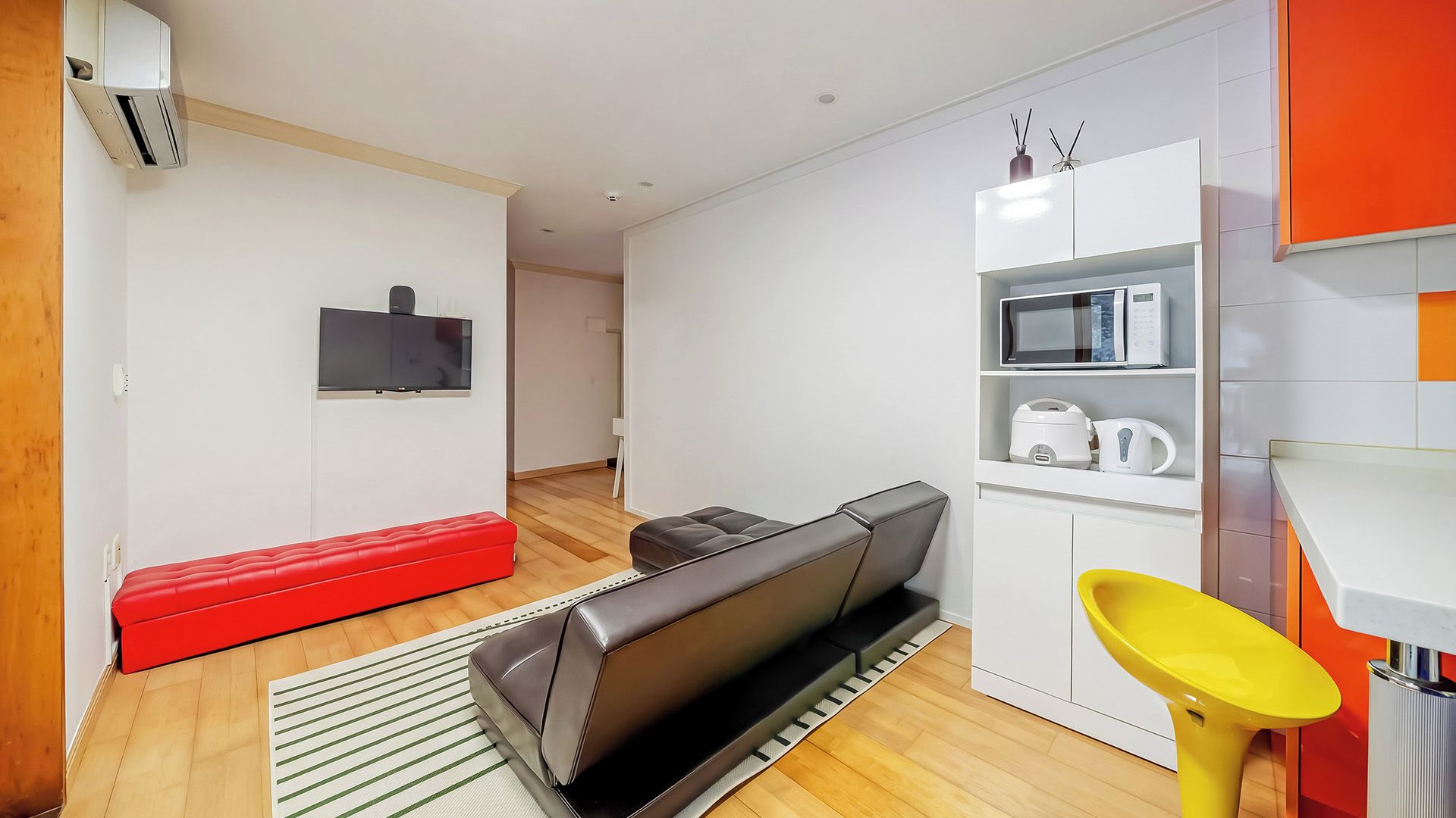 A compact living space with a sofa, a television, a microwave, and a small kitchen area.