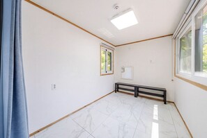 Une pièce aux murs blancs, dotée d’un sol en marbre, d’un luminaire au plafond, d’une fenêtre et d’un banc.