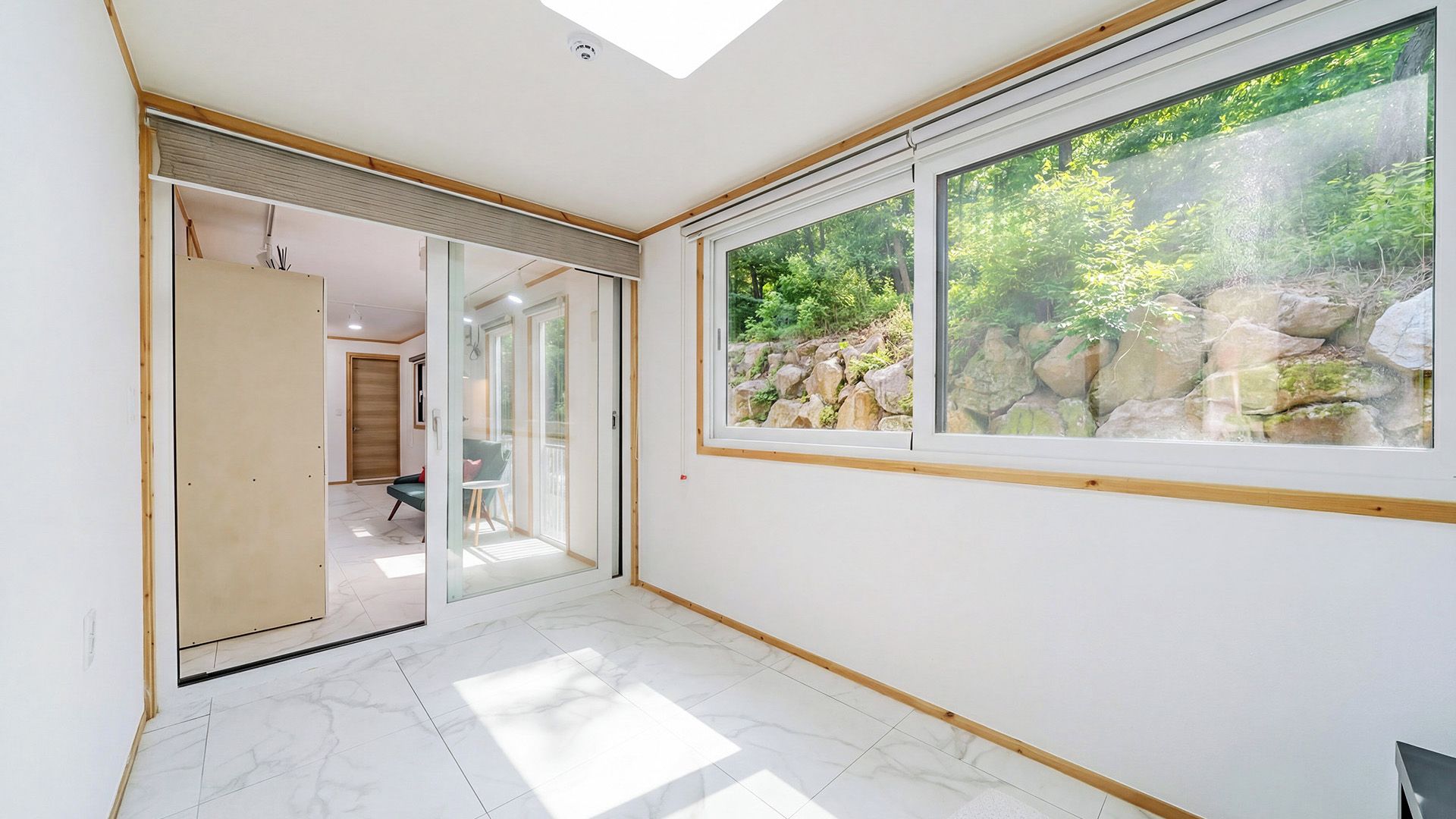 Un interior moderno con un ventanal grande, una puerta de cristal que da a otra habitación y suelo de baldosas.