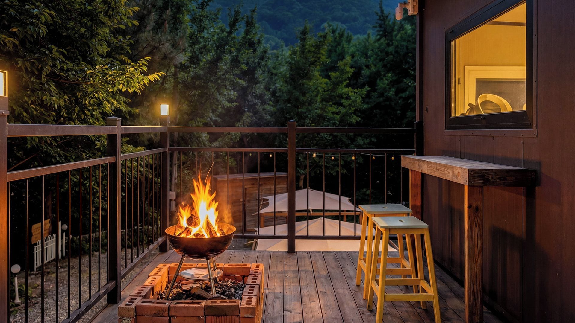 Una terraza de madera con un brasero, asientos al aire libre y vistas a un área boscosa.