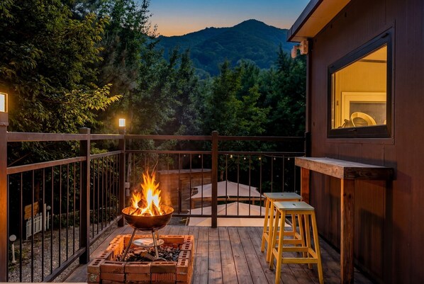 A deck with a fire pit, outdoor seating, and a view of a mountain. - Gapyeong Ruba Pension (Gapyeong)