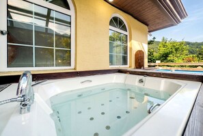 Uma banheira de hidromassagem com vista desobstruída da área circundante, incluindo uma piscina e uma casa com grandes janelas.