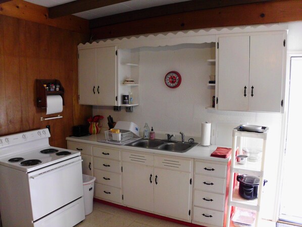 A kitchen with white cabinets, a stove, a sink, and a clock on the wall.