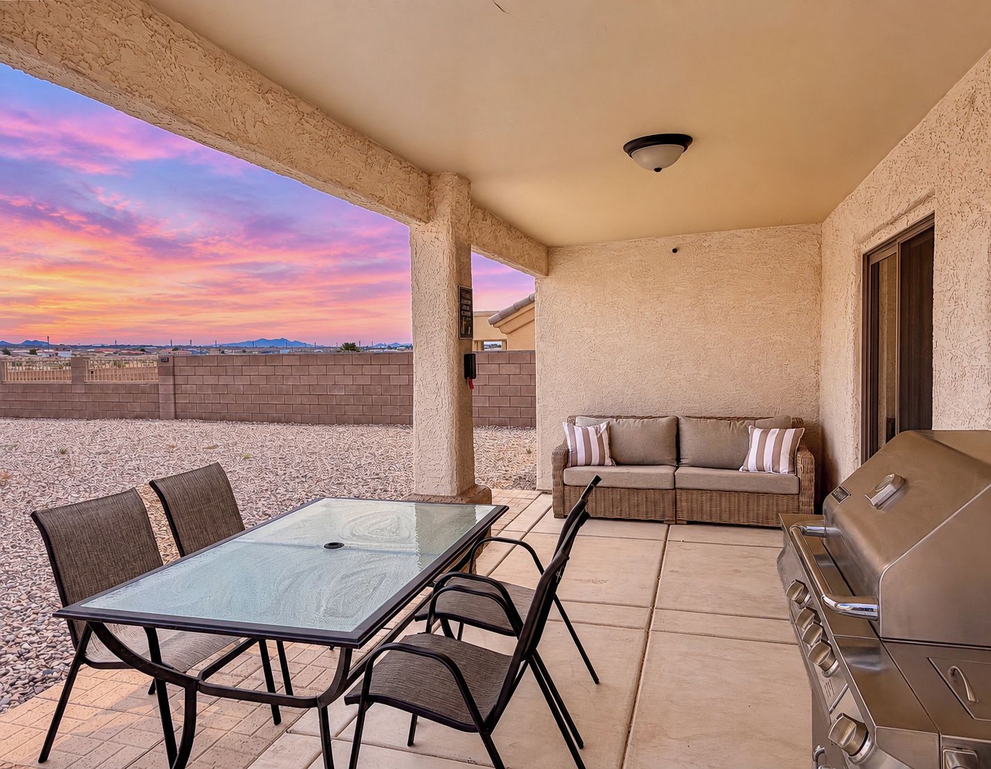 An outdoor patio with a glass table and chairs, a sofa, and a barbecue grill.