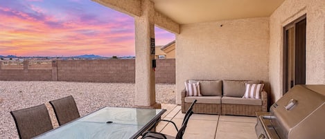 Une terrasse extérieure avec une table et des chaises en verre, un canapé et un barbecue.