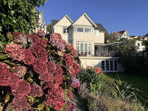 Uma casa de dois andares com varanda, rodeada por um jardim bem cuidado com hortênsias.