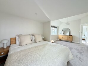 Een slaapkamer met een groot bed, een houten dressoir en een spiegel.