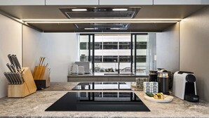 A modern kitchen with a central island, a built-in oven, and a window with a city view. - Brand New Apartment in Albert Park with Pool & Gym (Melbourne)