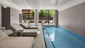 A modern indoor swimming pool with lounge chairs and a view of the outdoors. - Brand New Apartment in Albert Park with Pool & Gym (Melbourne)