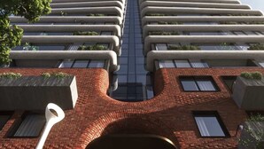 A modern building with a symmetrical facade, featuring a central glass section and multiple balconies with greenery. - Brand New Apartment in Albert Park with Pool & Gym (Melbourne)