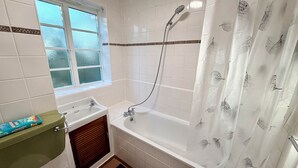 Un baño con bañera, ventana, lavabo e inodoro.