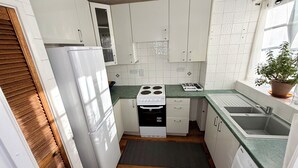Una cocina compacta con armarios blancos, una estufa, un lavamanos y una lavadora.