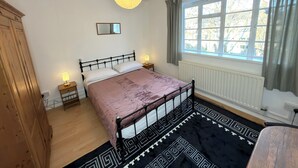 Un dormitorio con cama, lámparas de noche, una ventana con cortinas, un radiador y una lámpara colgante.