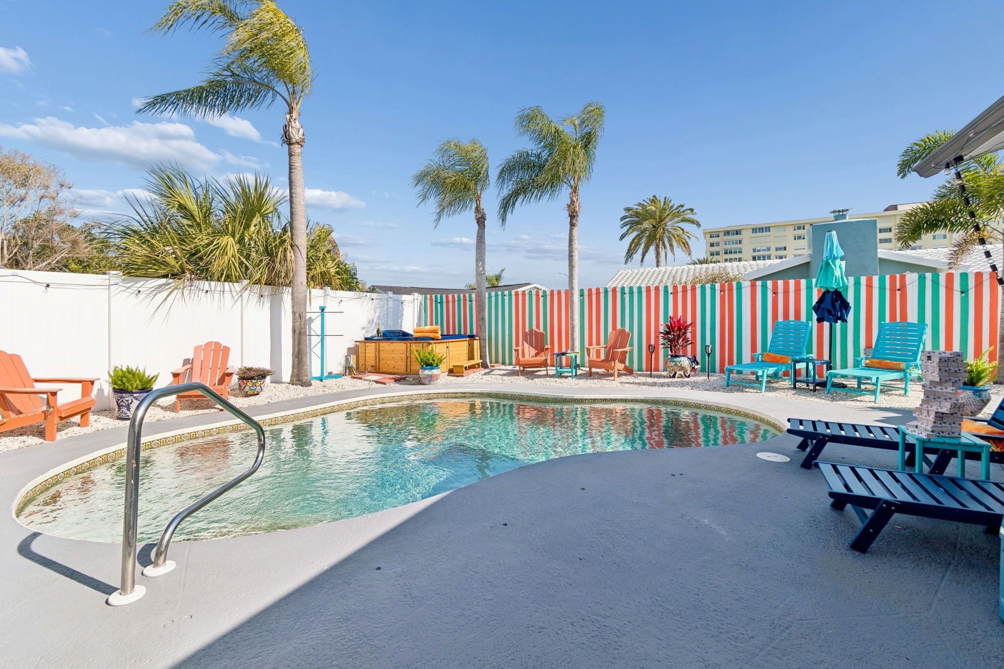 Un espace piscine avec des chaises longues, un petit jacuzzi et une clôture à rayures.