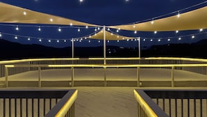 Une terrasse agrémentée de guirlandes lumineuses et surmontée d’un auvent, le tout entouré d’une rambarde.