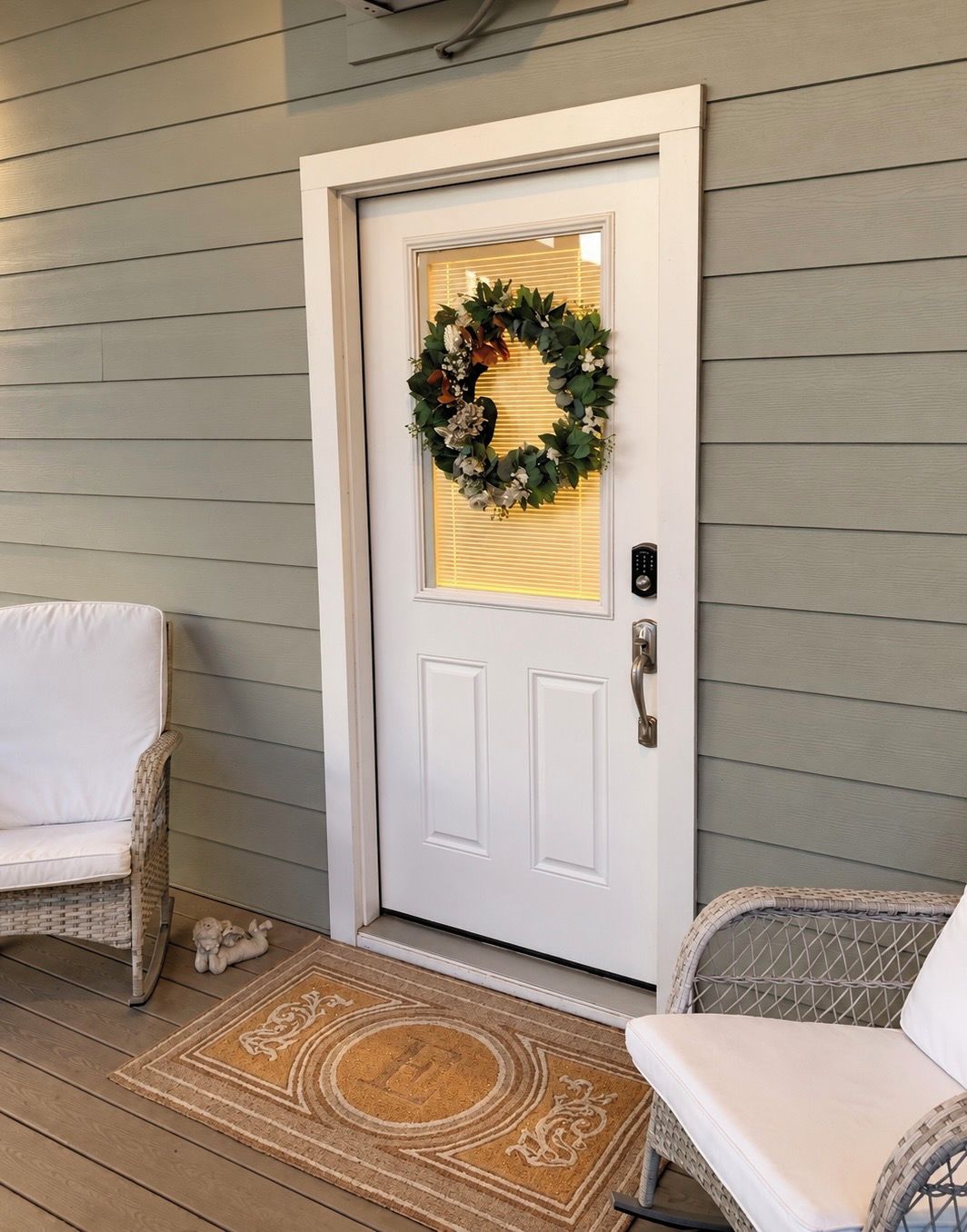 A front door with a wreath, a white chair, and a wicker chair outside.