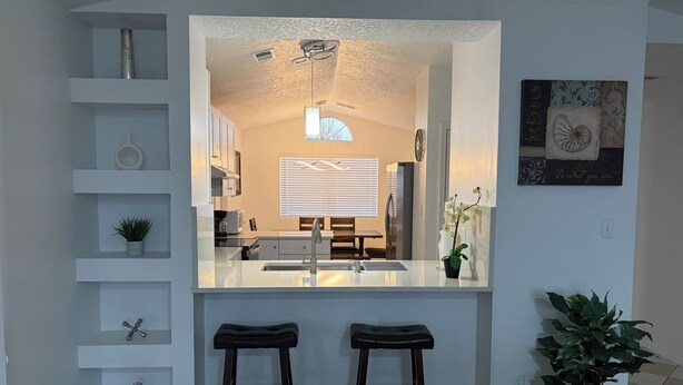 A modern kitchen with a central island, two stools, and a potted plant. - Newly Remodeled Mountain Escape Near Casino + Pool Table + Putting Green (Rio Rancho)