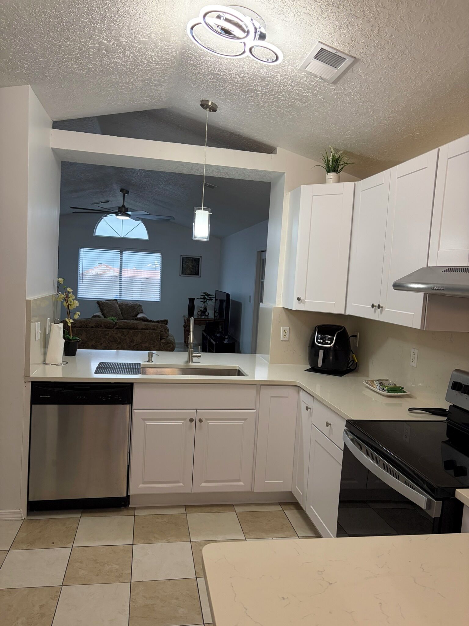A modern kitchen with white cabinets, a dishwasher, a stove, and a ceiling fan.