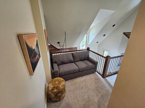 Un espacio habitable tipo loft con un sofá, un reposapiés estampado y un cuadro en la pared.