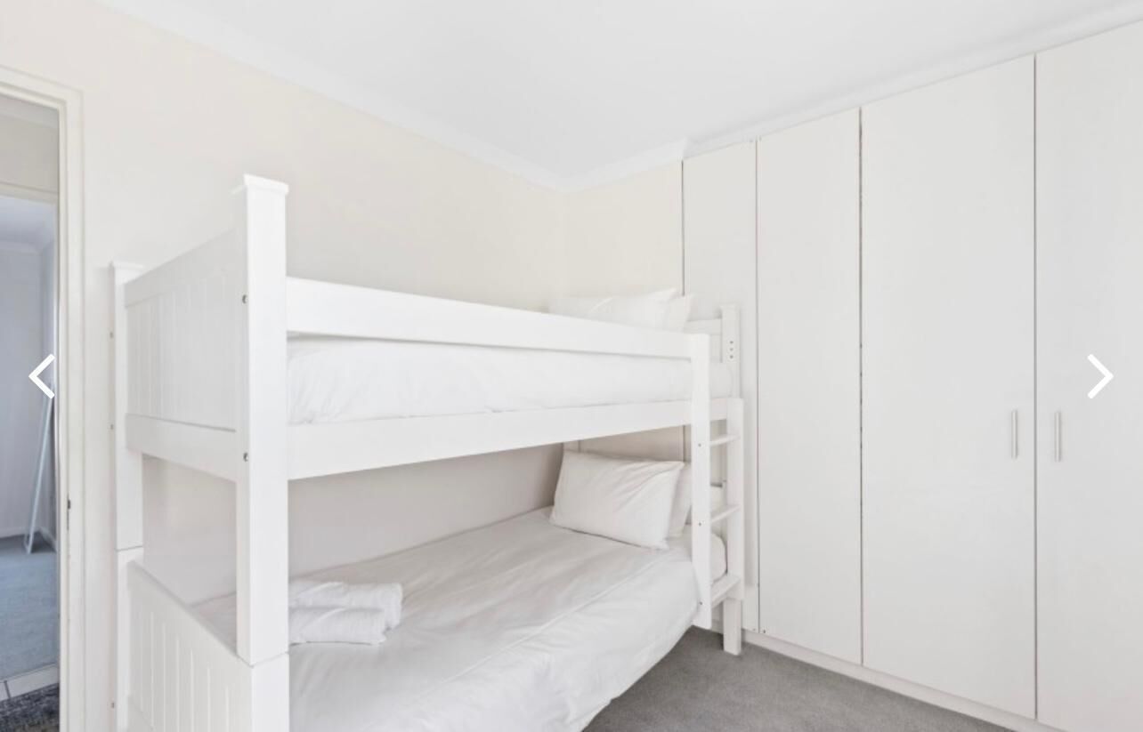 Uma cama beliche num quarto com paredes brancas e um guarda-roupa.