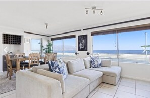 A modern living room with a large window offering a view of the beach. - An Exceptional Beachfront Retreat (Cape Town)