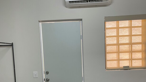 A room with a bed, a window with blinds, a door, and an air conditioning unit.