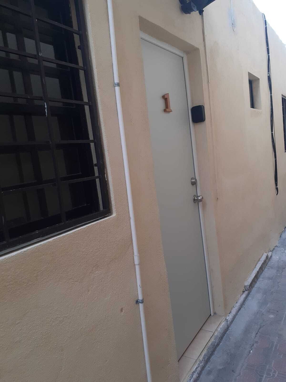 A beige building with a door marked '1', a barred window, and a small window on the right.