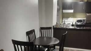 Ein kompakter Wohnbereich mit Essplatz, der ein dunkles Holztable und Stühle, eine Küchenzeile mit modernen Geräten sowie einen Holzboden umfasst.