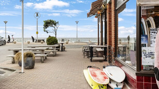 Ein Küstenrestaurant mit Außenbereich, Blick auf das Meer und Surfbrettern, die draußen ausgestellt sind.