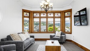 Ein Zimmer mit Erkerfenster, zwei grauen Sofas, einem Holztisch und einer Chandelier.