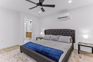 Une chambre à coucher comprenant un lit, un ventilateur de plafond, un climatiseur et une table de chevet avec une lampe.