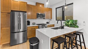 Una cocina moderna con armarios de madera, electrodomésticos de acero inoxidable, una isla de mármol blanco y taburetes de bar.