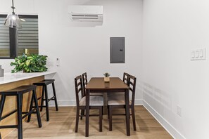 Un coin repas avec une table et des chaises en bois, un appareil de climatisation, un luminaire et une petite plante posée sur le comptoir.