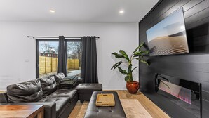 Una sala de estar moderna con un sofá de cuero, una mesa de centro de madera y un televisor de pantalla plana grande montado en una pared oscura.