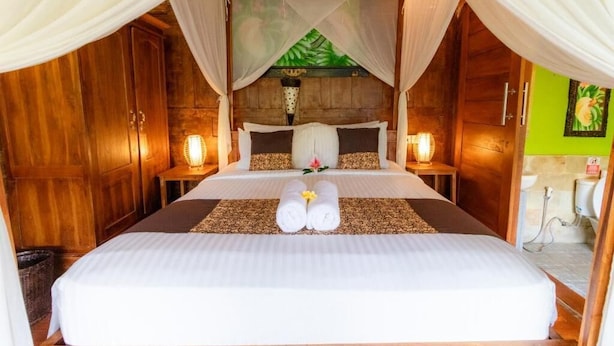 A bedroom with a canopy bed, wooden walls, and a green leaf mural. - Room-deluxe Bungalow at Doni House (Ubud)