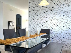 Ein moderner Essbereich mit einem Glastisch, schwarzen Stühlen und einer Wand mit geometrischem Muster.
