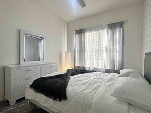 Ein Schlafzimmer mit Bett, Schminktisch, Spiegel und einem Fenster mit Vorhängen.