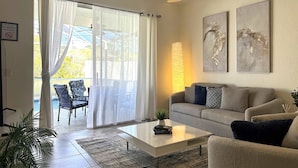 A living room with a sofa, coffee table, and chairs. There is a sliding glass door leading to an outdoor area. - Family Villa 5 bedroom near disney world 5 Villa (Davenport)