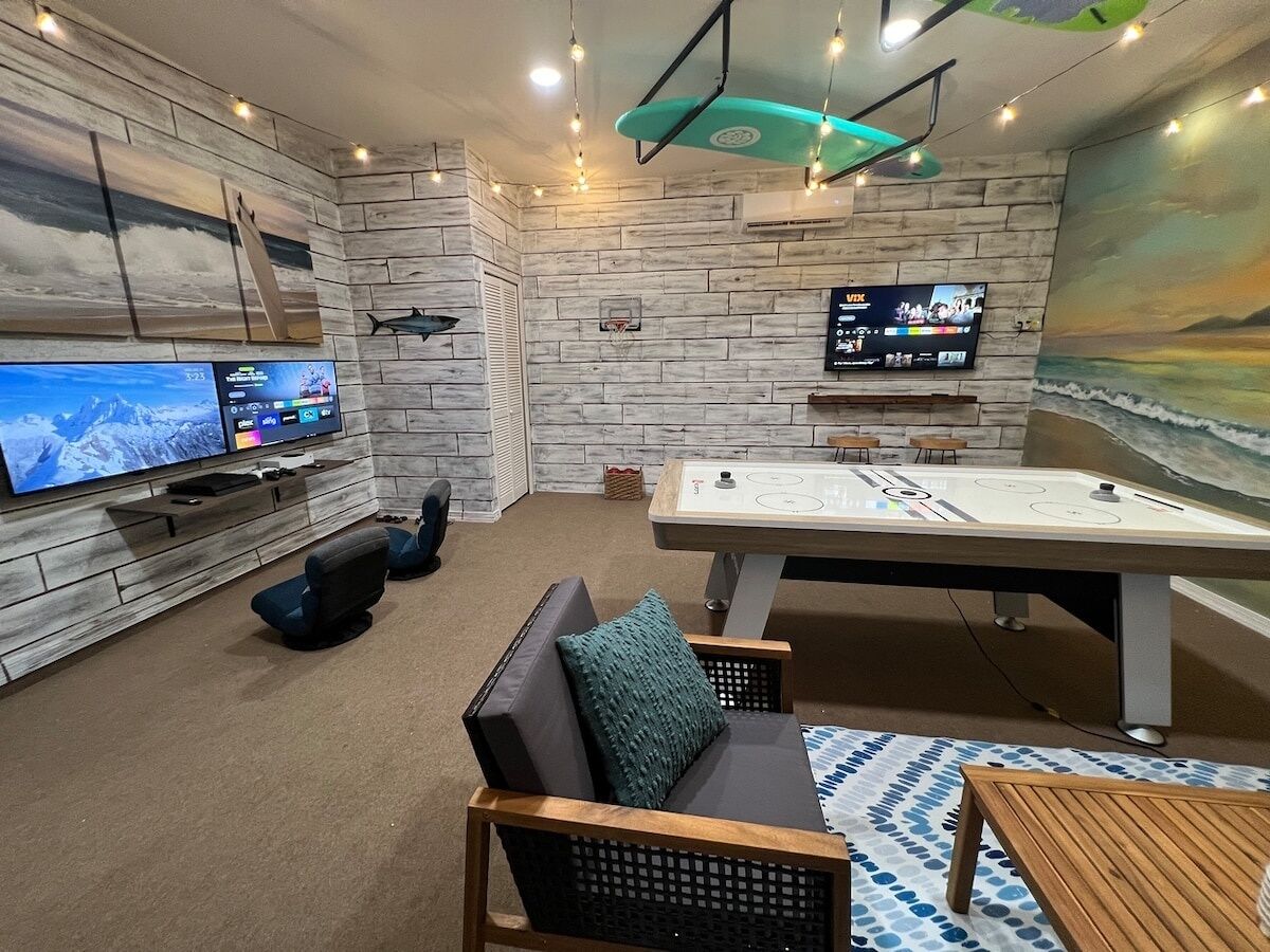 Een kamer met een pooltafel, een flatscreen-tv en een zithoek met een bank en stoelen.