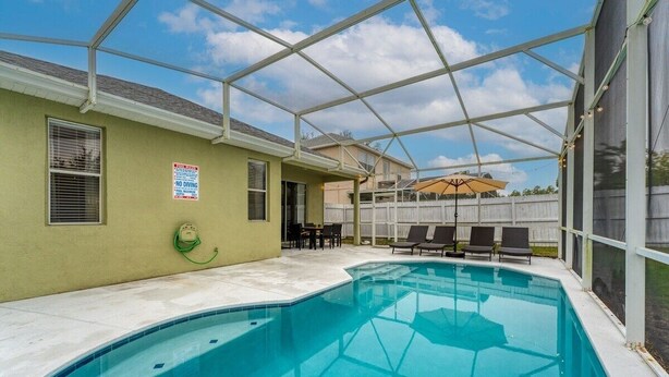 Una piscina con un patio techado, un letrero que indica 'No Diving' y un jardín trasero cercado.